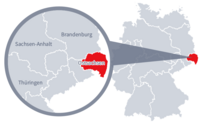 Diese Grafik zeigt eine Karte von Deutschland mit einer detaillierten Ansicht der Region Ostsachsen. Ostsachsen ist in Rot hervorgehoben und liegt im östlichen Teil Deutschlands. Ein Lupensymbol vergrößert diesen Bereich, um die Lage genauer darzustellen. 